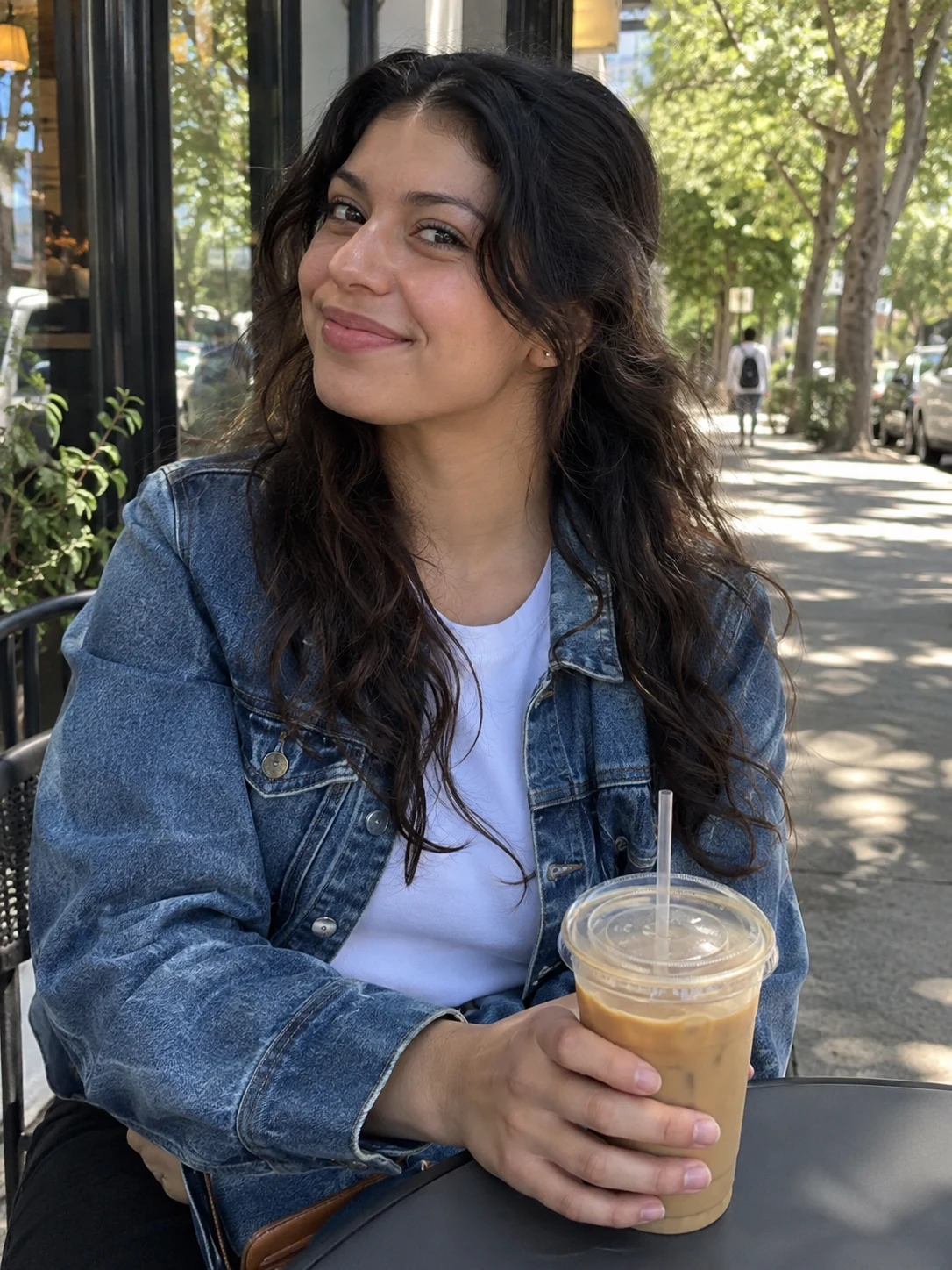 Adult fictional woman with iced coffee outside a neighborhood cafe